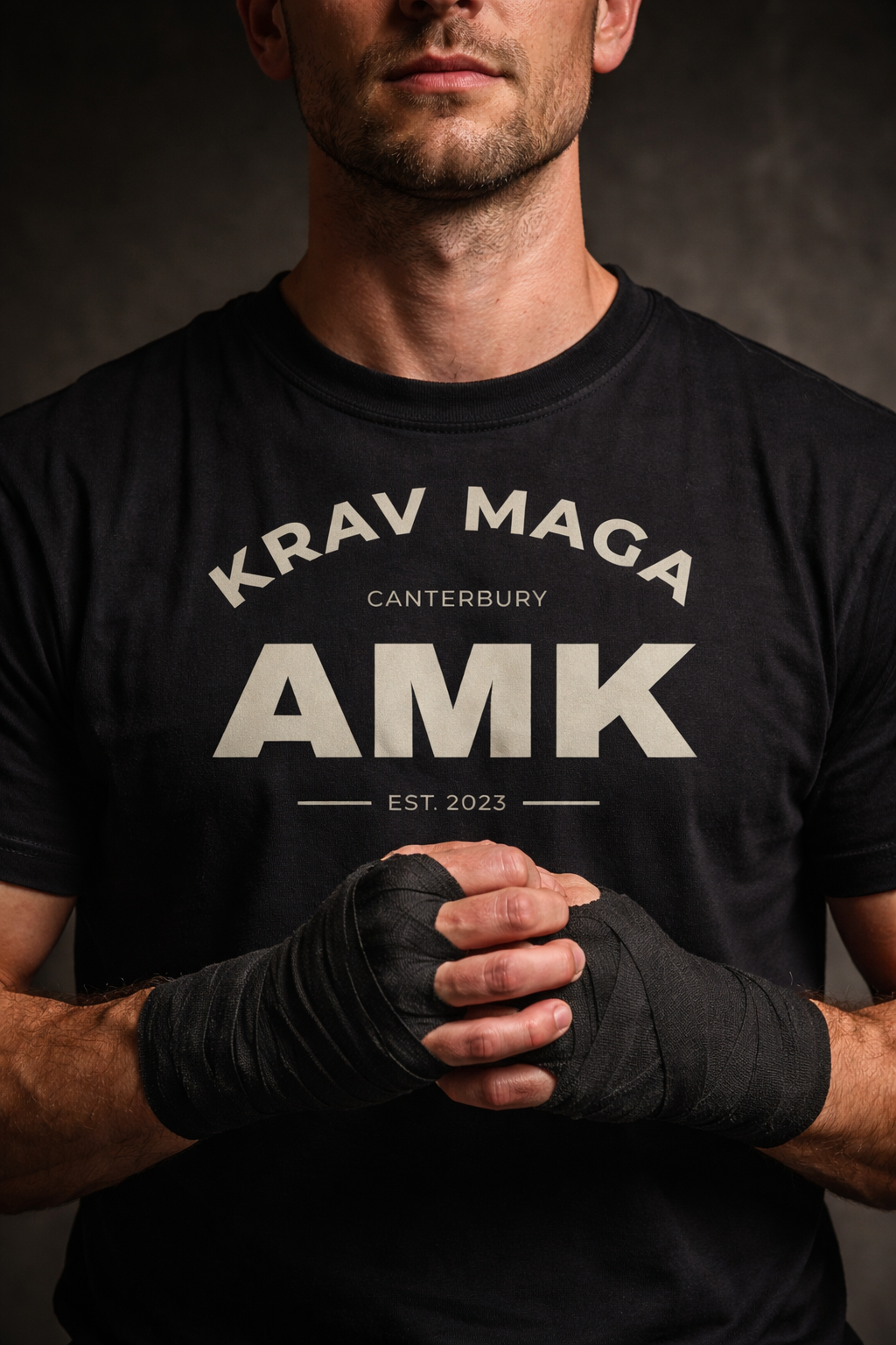 Person wearing a black 'Krav Maga Canterbury AMK' t-shirt with black hand wraps